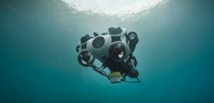 Unterwasser-Roboter mit Kameralinse und Propellern schwimmt im klaren Wasser nahe der Oberfläche.